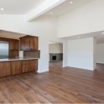 Spacious modern kitchen with wooden cabinets and flooring, featuring stainless steel appliances and an adjoining living area with a fireplace.