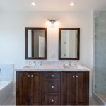 Modern bathroom featuring dual mirrors, dark wood vanity, white countertop, bathtub, and walk-in shower with glass door.