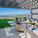 Outdoor patio area with wicker furniture under a pergola, overlooking a scenic view of a cityscape and mountains.