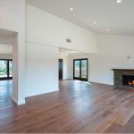 Spacious, modern living room with hardwood floors, white walls, recessed lighting, a stone fireplace, and large windows.