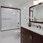 A bathroom with white tile and brown cabinets.