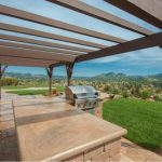 Outdoor patio area with a pergola covering and a built-in barbecue grill, overlooking a scenic view of green hills and clear skies.