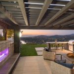 Outdoor patio with a fireplace, seating area, and dining table, overlooking a scenic sunset view of hills and a lake.
