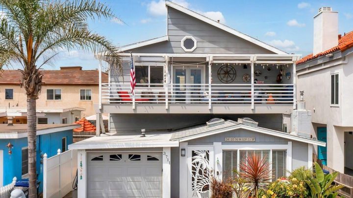 Spacious two-story beach house with balcony and garage under a blue sky.