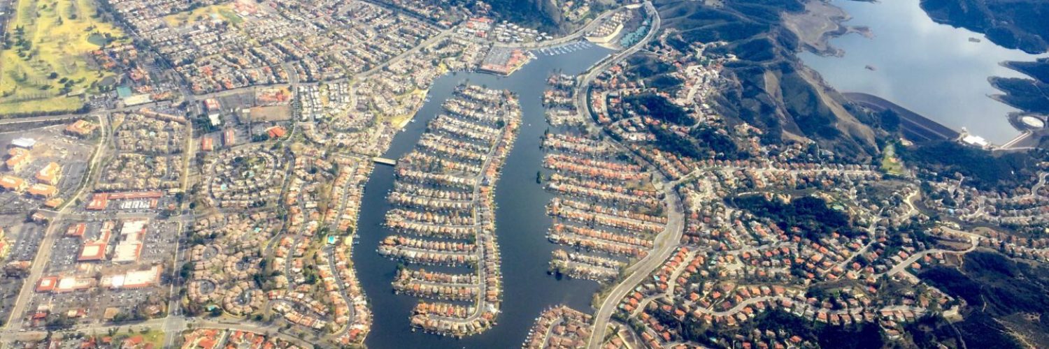 Aerial view of a luxury residential area in Westlake Village, CA, with winding waterways and distinct housing layouts, surrounded by hills and larger bodies of water.